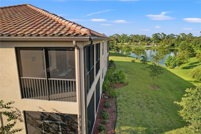 view of property exterior featuring a sunroom, a lawn, and a water view