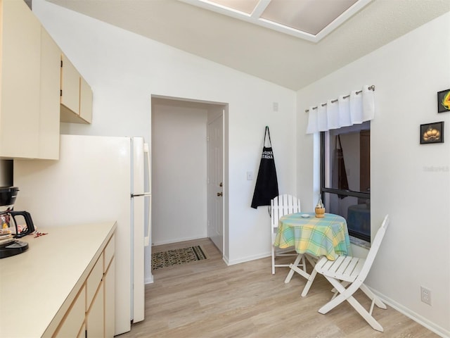 kitchen featuring light wood-type flooring, cream cabinetry, vaulted ceiling, and white refrigerator