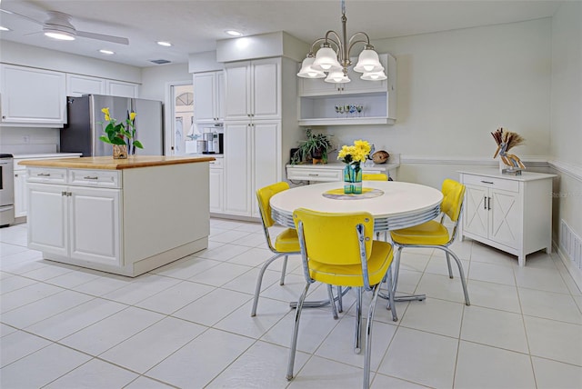 kitchen with appliances with stainless steel finishes, light tile patterned flooring, a kitchen island, white cabinetry, and decorative light fixtures