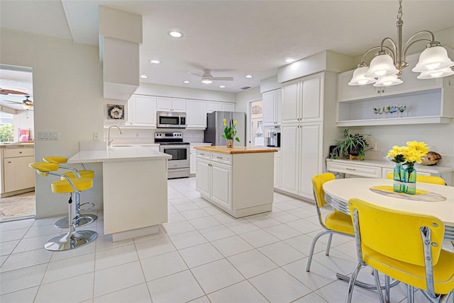 kitchen with hanging light fixtures, kitchen peninsula, white cabinetry, light tile patterned floors, and appliances with stainless steel finishes