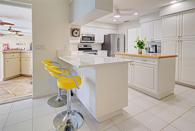 kitchen featuring appliances with stainless steel finishes, kitchen peninsula, a breakfast bar area, white cabinetry, and light tile patterned floors