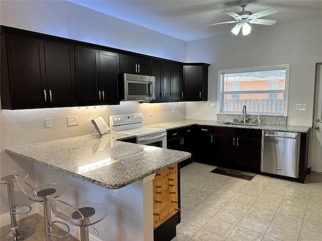 kitchen with light stone countertops, sink, stainless steel appliances, kitchen peninsula, and a breakfast bar area