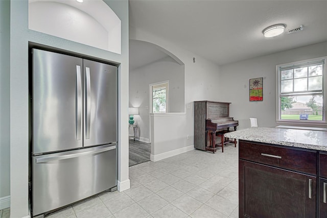 kitchen featuring stainless steel fridge, dark brown cabinets, light tile patterned floors, and a healthy amount of sunlight