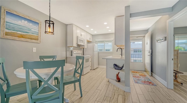 kitchen with decorative light fixtures, white cabinets, sink, and white appliances