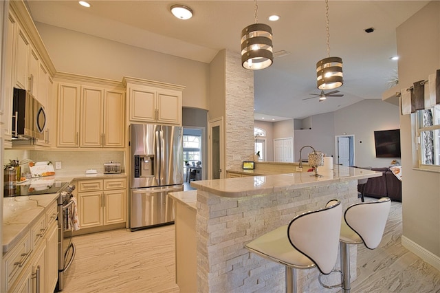 kitchen featuring a breakfast bar area, vaulted ceiling, appliances with stainless steel finishes, light stone countertops, and ceiling fan