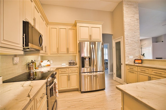 kitchen with appliances with stainless steel finishes, decorative backsplash, cream cabinetry, light stone countertops, and light wood-type flooring