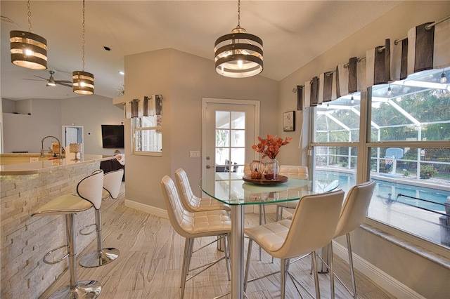 dining space with light wood-type flooring, ceiling fan with notable chandelier, lofted ceiling, and sink