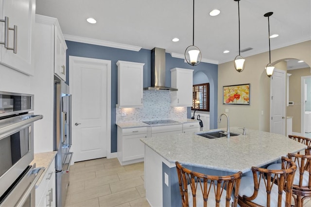 kitchen featuring hanging light fixtures, wall chimney exhaust hood, white cabinetry, and sink