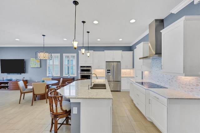 kitchen featuring sink, wall chimney exhaust hood, a kitchen island with sink, white cabinetry, and stainless steel appliances