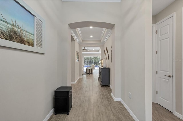 hallway with ornamental molding, a raised ceiling, and light hardwood / wood-style floors