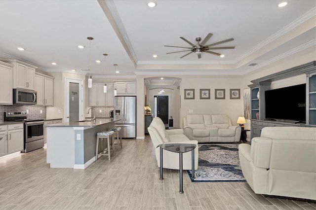 living room featuring ceiling fan, ornamental molding, sink, a tray ceiling, and light hardwood / wood-style floors