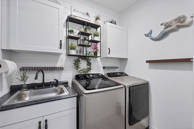 clothes washing area featuring sink, washing machine and clothes dryer, and cabinets