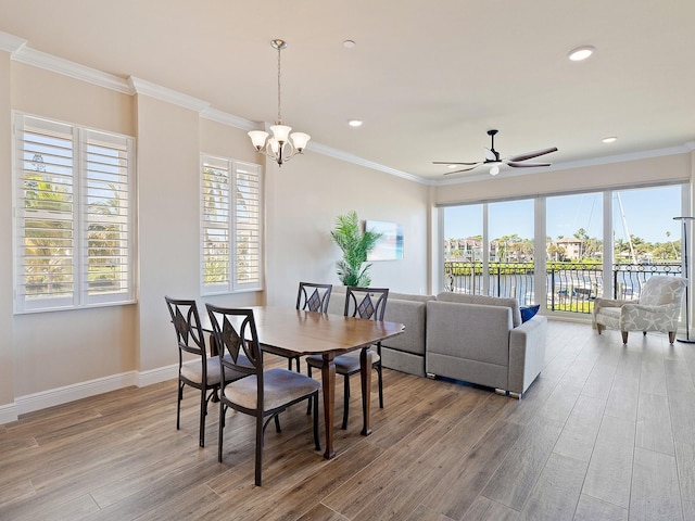 dining space with ceiling fan with notable chandelier, a water view, ornamental molding, and hardwood / wood-style flooring