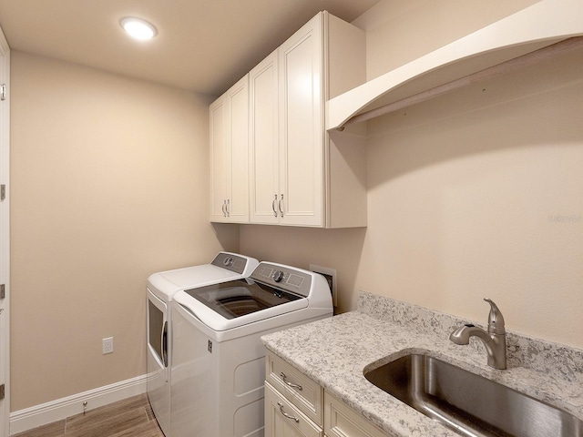 laundry area featuring cabinets, washing machine and dryer, light hardwood / wood-style flooring, and sink