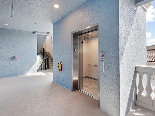 hall with carpet floors, a textured ceiling, and elevator