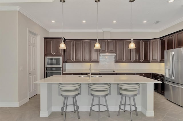 kitchen with stainless steel appliances, dark brown cabinetry, decorative light fixtures, a center island with sink, and sink