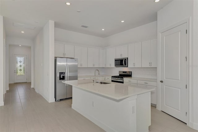 kitchen featuring sink, white cabinets, stainless steel appliances, backsplash, and a center island with sink