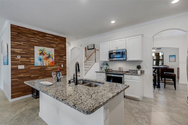 kitchen featuring wood walls, sink, a kitchen island with sink, white cabinetry, and stainless steel appliances