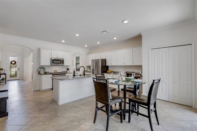 kitchen with appliances with stainless steel finishes, white cabinetry, light stone countertops, a center island with sink, and sink