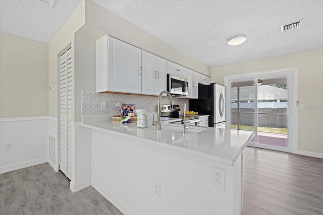 kitchen with white cabinets, kitchen peninsula, a textured ceiling, light hardwood / wood-style flooring, and appliances with stainless steel finishes