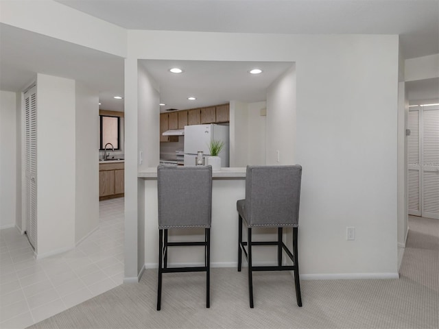 kitchen featuring light colored carpet, sink, white fridge, and kitchen peninsula