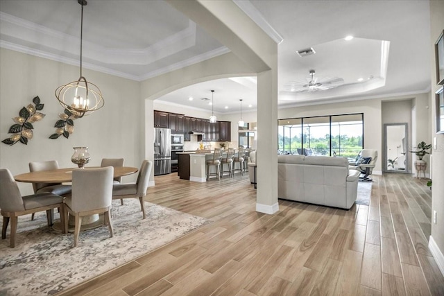 dining area featuring ornamental molding, ceiling fan with notable chandelier, a tray ceiling, and light hardwood / wood-style floors