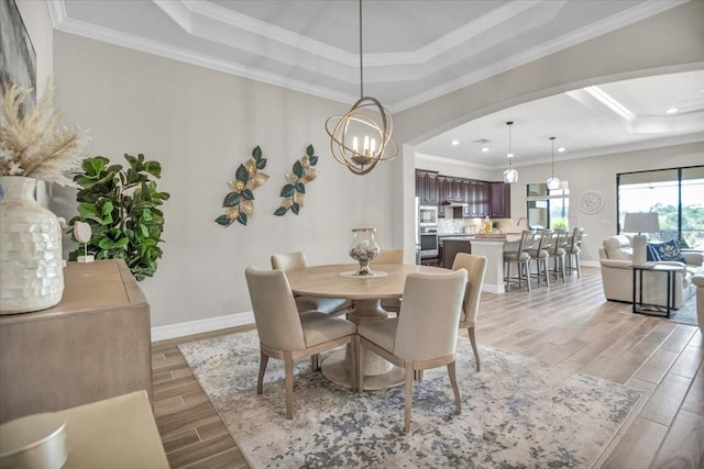 dining area with a raised ceiling, ornamental molding, light hardwood / wood-style flooring, and a chandelier