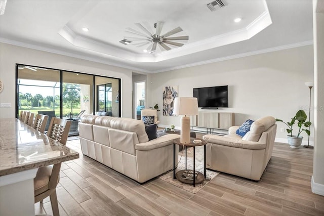 living room featuring light hardwood / wood-style floors, a raised ceiling, ornamental molding, and ceiling fan