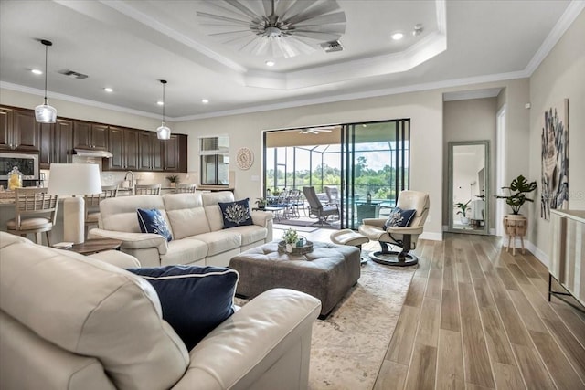 living room with light hardwood / wood-style flooring, ornamental molding, and a tray ceiling