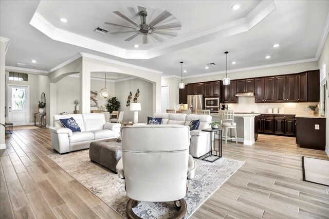 living room with light hardwood / wood-style flooring, crown molding, a tray ceiling, and ceiling fan