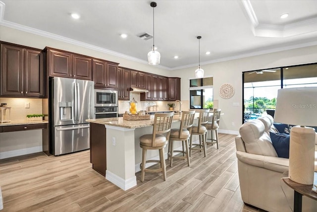 kitchen with an island with sink, a breakfast bar, decorative light fixtures, light wood-type flooring, and appliances with stainless steel finishes