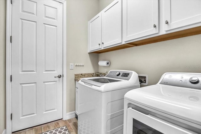 laundry room featuring washer and clothes dryer, light hardwood / wood-style flooring, and cabinets