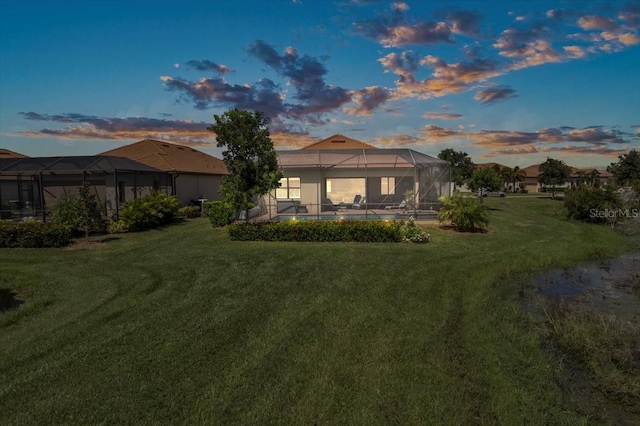 back house at dusk featuring a yard, glass enclosure, and a swimming pool