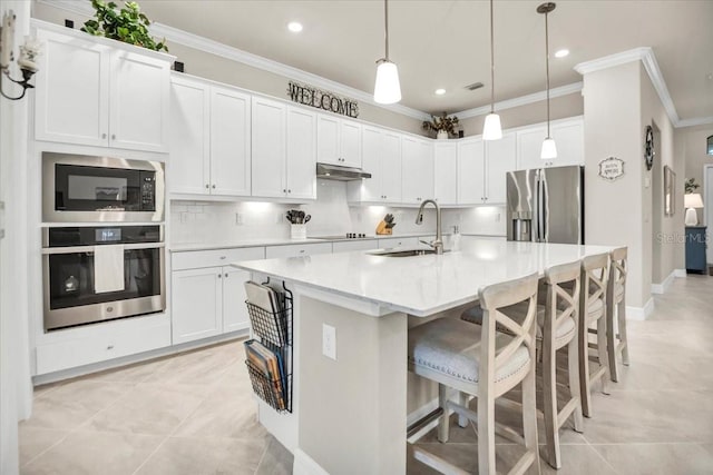 kitchen with white cabinetry, stainless steel appliances, decorative light fixtures, and an island with sink