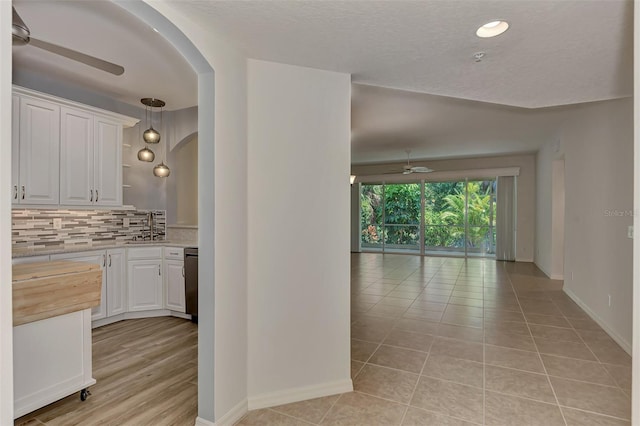 kitchen with hanging light fixtures, light tile patterned floors, backsplash, white cabinetry, and dishwasher