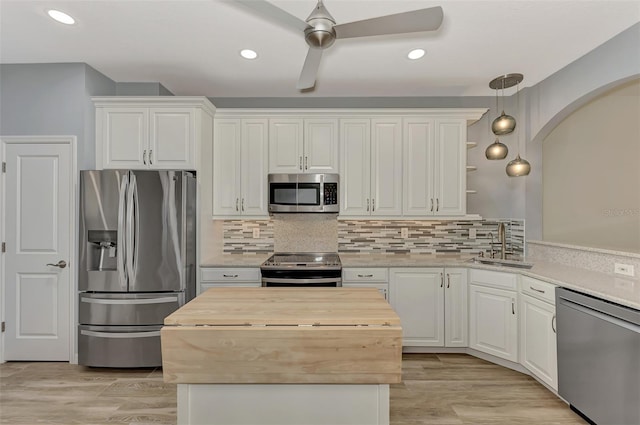 kitchen with appliances with stainless steel finishes, hanging light fixtures, white cabinetry, butcher block counters, and light wood-type flooring