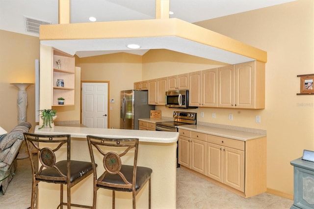 kitchen with appliances with stainless steel finishes, vaulted ceiling, a breakfast bar, kitchen peninsula, and light brown cabinets