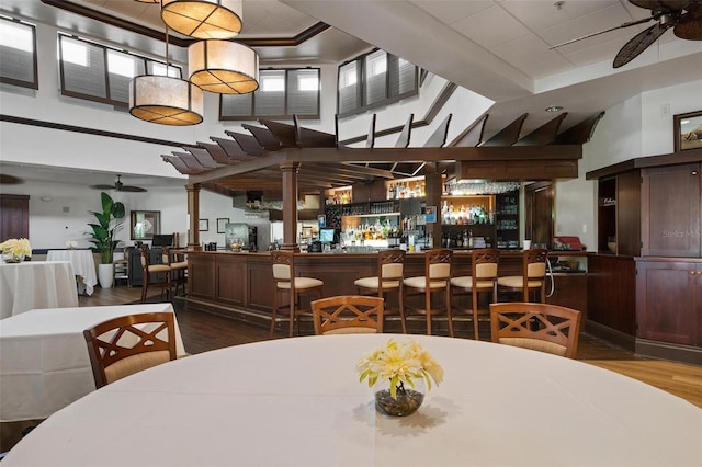 dining space with ceiling fan, a towering ceiling, wood-type flooring, and indoor bar