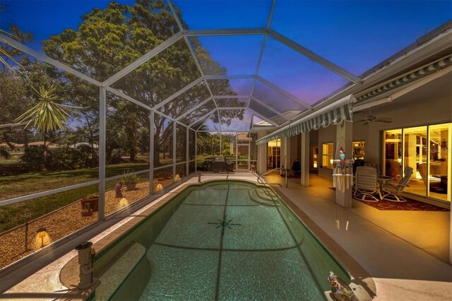 pool at dusk with a patio, glass enclosure, and ceiling fan