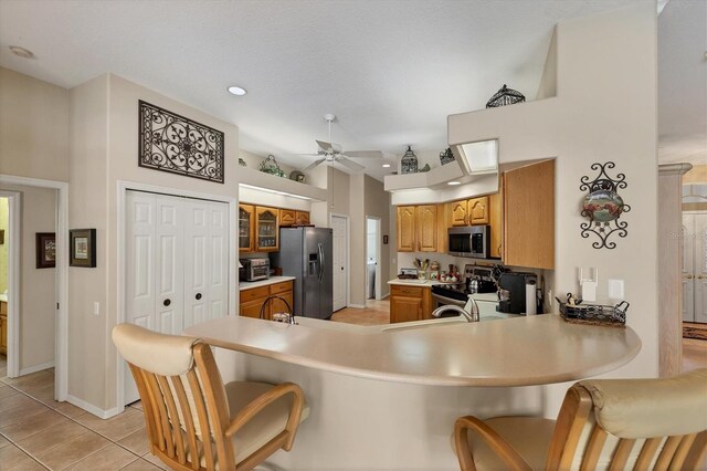 kitchen featuring kitchen peninsula, appliances with stainless steel finishes, light tile patterned floors, a high ceiling, and ceiling fan