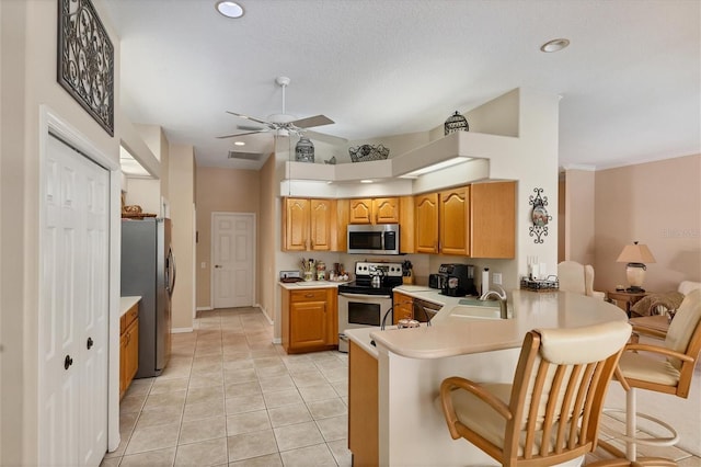 kitchen with appliances with stainless steel finishes, a breakfast bar, kitchen peninsula, light tile patterned floors, and ceiling fan