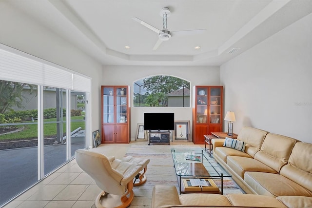 living room with a raised ceiling, light tile patterned floors, and ceiling fan