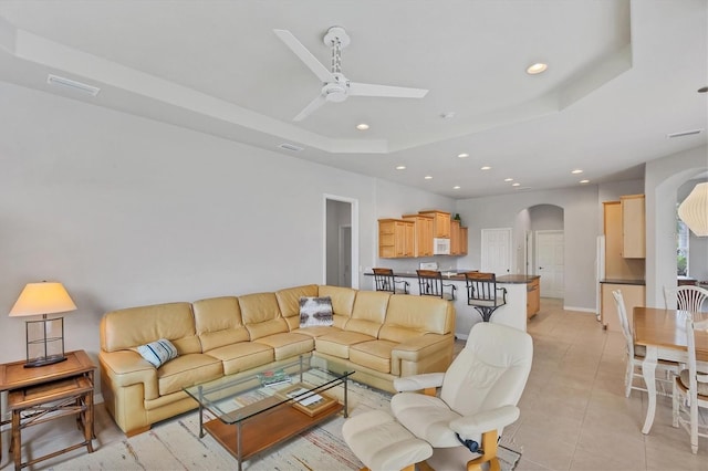 tiled living room with ceiling fan and a raised ceiling