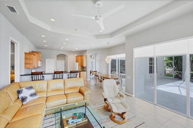 tiled living room featuring ceiling fan and a raised ceiling