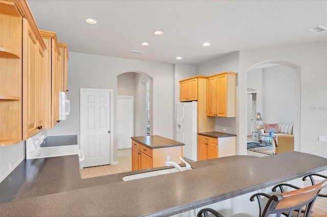 kitchen with white appliances, kitchen peninsula, light brown cabinets, and sink