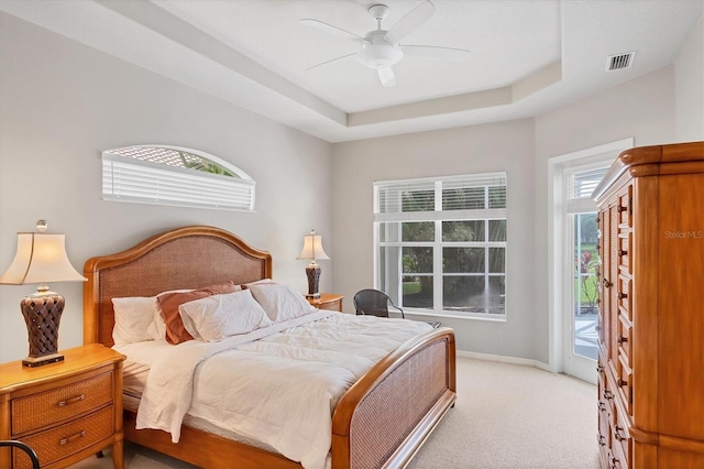 carpeted bedroom with ceiling fan, a raised ceiling, and access to exterior