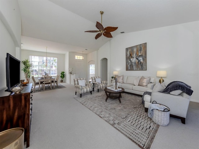 carpeted living room with ceiling fan with notable chandelier and vaulted ceiling