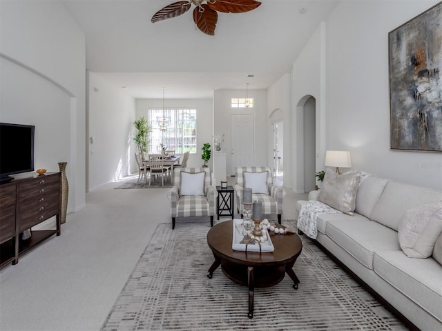 carpeted living room with a high ceiling and ceiling fan with notable chandelier