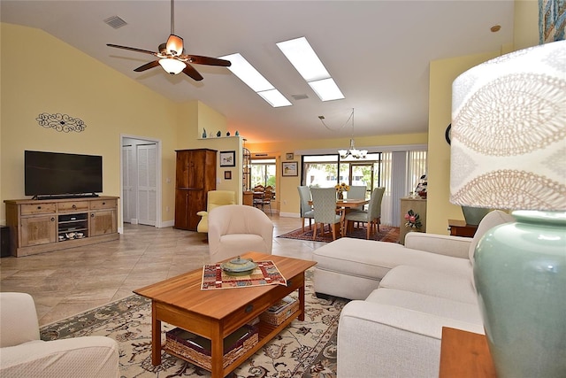 living room with ceiling fan with notable chandelier, light tile patterned flooring, a skylight, and high vaulted ceiling