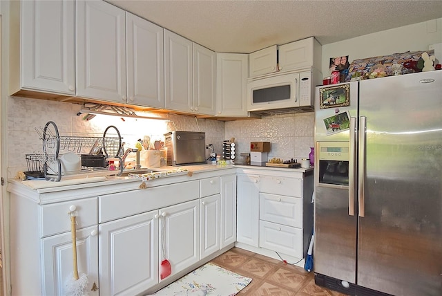 kitchen with a textured ceiling, stainless steel fridge, decorative backsplash, and white cabinets